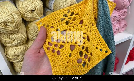 Main tenant un échantillon de tissu en dentelle au crochet jaune vif avec motif floral dans une boutique de fil Banque D'Images