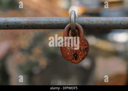 Cadenas rouillé en forme de cœur verrouillé sur un câble de pont métallique. Concept de romance, de nostalgie, du temps qui passe et de durabilité Banque D'Images