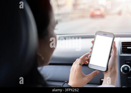 Vue arrière d'une jeune femme asiatique assise dans la voiture et conduisant en ville. Femme utilisant la navigation sur un téléphone portable ou certaines applications. Banque D'Images