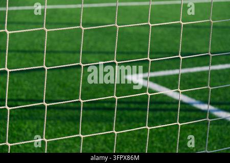 Vue rapprochée d'un filet de football blanc traversant un terrain en gazon artificiel vert vif, avec des marquages de limite lumineux qui s'entrecroisent visibles à travers le maillage Banque D'Images