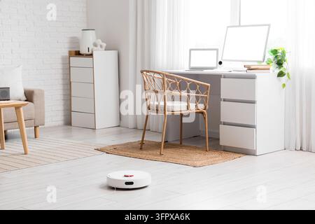 Automatisation de la maison intelligente et nettoyage domestique, aspirateur robotique travaillant dans un bureau à domicile moderne et lumineux avec configuration de travail à distance et décor minimaliste Banque D'Images