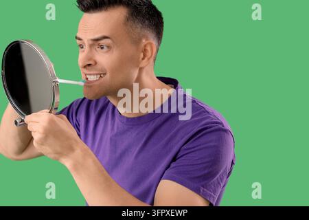Hygiène bucale et soins dentaires, homme se brossant les dents devant un miroir pour sa routine quotidienne de santé et ses habitudes de bien-être sur un fond vert Banque D'Images