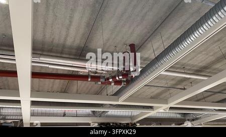 Conduits de ventilation exposés et tuyaux industriels installés sous un plafond en béton dans un bâtiment commercial moderne Banque D'Images