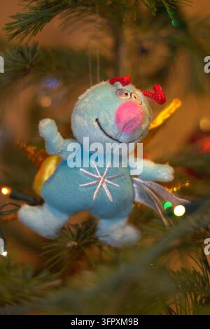 Un plan vertical rapproché détaillé d'une poupée en peluche bleue drôle accrochée à un sapin de Noël à l'intérieur. Banque D'Images
