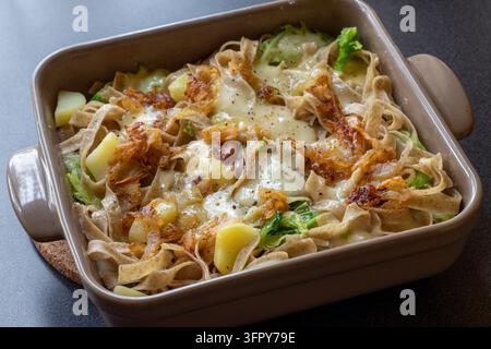 Vue aérienne de pizzoccheri cuits au four avec des pommes de terre, du chou, du fromage fondu et des oignons frits dans un plat de cuisson en céramique brune, lumière naturelle douce Banque D'Images