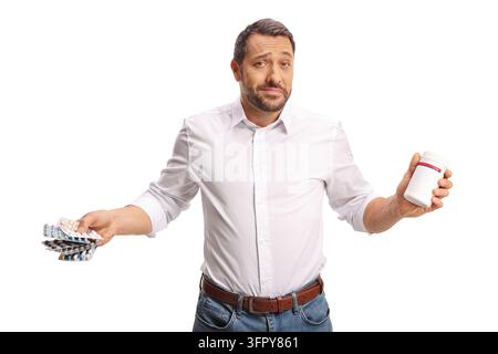 Homme confus tenant plusieurs paquets de pilules dans une main et un flacon de médicament dans l'autre, isolé sur fond blanc Banque D'Images