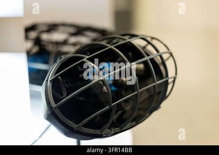 Microphone cylindrique noir avec une grille métallique arrondie remplit le premier plan, tandis qu'un autre microphone et une fenêtre lumineuse restent légèrement flous en arrière-plan Banque D'Images