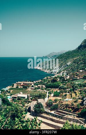 Une vue aérienne d'un paysage côtier en terrasses à Majorque, en Espagne, présentant des maisons traditionnelles, une végétation luxuriante et des vignobles qui descendent en cascade Banque D'Images