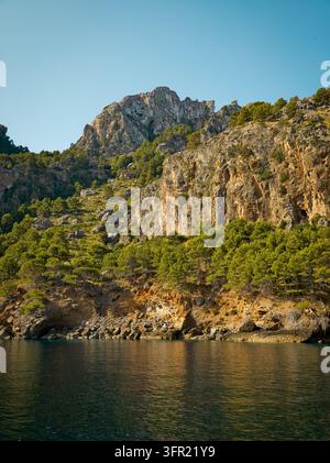 Un plan vertical mettant en valeur les montagnes rocheuses accidentées ornées de denses forêts de pins verts, rencontrant les eaux calmes et réfléchissantes de la Méditerranée Banque D'Images