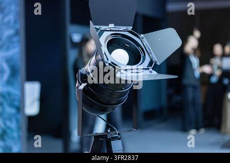 Amsterdam, Pays-Bas – 11 septembre 2026 : Un projecteur professionnel avec volets réglables se trouve au premier plan, tandis que les visiteurs et l’exposition Banque D'Images