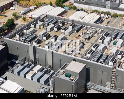 Grand bâtiment industriel de centre de données avec de nombreux ventilateurs de refroidissement et systèmes de climatisation sur le toit, entouré de zones de stationnement et de structures d'entrepôt Banque D'Images