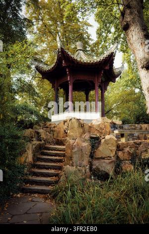 Pavillon chinois traditionnel en bois construit sur une formation rocheuse avec des marches en pierre dans le Bethmannpark de Francfort entouré d'arbres d'automne Banque D'Images