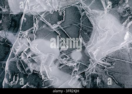 Macro détaillée d'un lac gelé naturel montrant des motifs de givre complexes, des bulles d'air et des fissures cristallines profondes sur une surface hivernale froide Banque D'Images