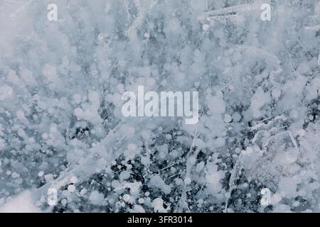 Macro détaillée de bulles de méthane blanc gelées et de fissures piégées sous une glace bleue claire en hiver dans l'oblast d'Irkoutsk, en Russie, montrant la texture naturelle Banque D'Images
