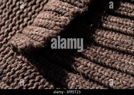 Tissu de laine tricoté brun montrant la texture et les détails, créant un fond chaleureux et douillet avec des ombres et de la lumière Banque D'Images