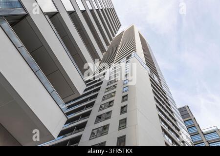 Une vue en contre-plongée dirigée vers le haut vers des immeubles d'habitation imposants et des balcons, contre un ciel bleu clair parsemé de nuages vaporeux Banque D'Images