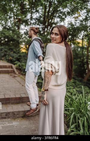 Photo en extérieur d'un jeune couple amoureux marchant sur un sentier à travers un champ de prairies. Jeune couple se promenant dans le parc. Couple tendance avec des tatouages marchant dans Banque D'Images