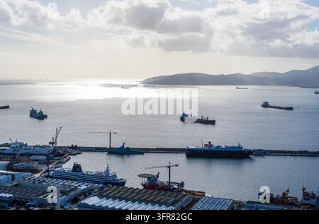 Une vue panoramique sur le port de Gibraltar montre plusieurs cargos et ferries dans la baie, avec des installations portuaires industrielles et des grues le long du front de mer Banque D'Images