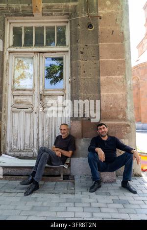 Hommes assis sur un banc en pierre à côté d'une vieille porte en bois patinée, province de Shirak, Gyumri, Arménie Banque D'Images