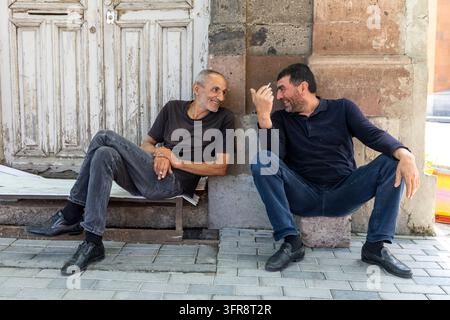 Deux hommes âgés discutant et fumant assis sur un banc devant une vieille porte en bois, province de Shirak, Gyumri, Arménie Banque D'Images