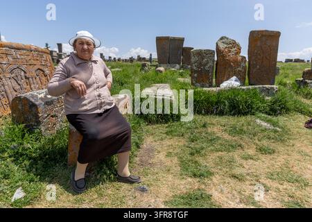 Femme assise parmi des khatchkars sculptés au cimetière médiéval de Noratus, province de Gegharkunik, Noratus, Arménie Banque D'Images