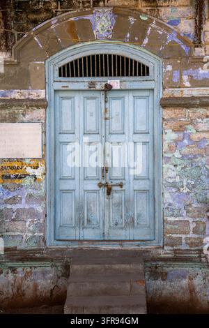 Une porte en bois à panneaux bleu clair est encadrée par une arche en pierre au sommet de marches usées, Gujarat, Mandvi, Inde Banque D'Images