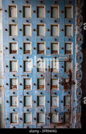Une vue rapprochée montre la texture érodée d'une porte en bois à panneaux bleus avec des clous métalliques et une serrure en fer, Gujarat, Mandvi, Inde Banque D'Images