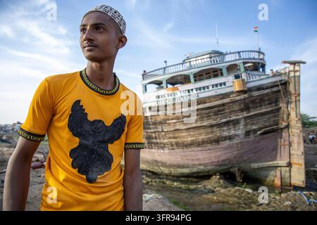 Jeune homme portant une casquette debout à côté d'un grand cargo en bois échoué, Gujarat, Mandvi, Inde Banque D'Images