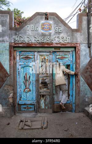 Homme vêtu de blanc franchissant une porte en bois bleu patiné ornée d'une inscription gujarati, Gujarat, Mandvi, Inde Banque D'Images