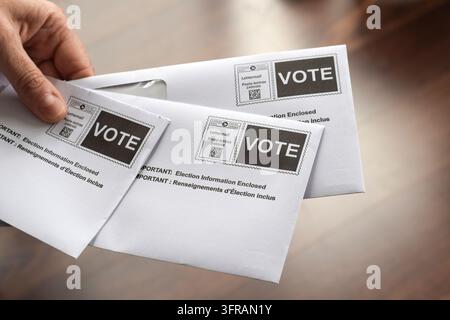 Aurora, Ontario, Canada – 8 octobre 2026 : Gros plan d'une main tenant des enveloppes d'information sur le vote canadien marquées « VOTE » Banque D'Images