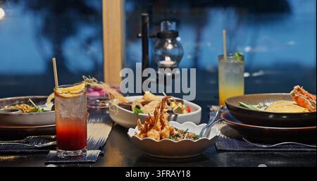 Dîner gastronomique thaïlandais avec vue sur la mer au coucher du soleil. Délicieux plats de fruits de mer gastronomiques et cocktails rafraîchissants sur la table dans un restaurant tropical de luxe. Rome Banque D'Images