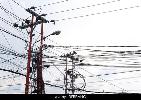 Câbles et fils électriques emmêlés sur des poteaux électriques avec des isolateurs et un lampadaire sous un ciel nuageux Banque D'Images