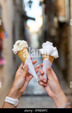 Close up de deux mains tenant de délicieuses boules de gelato crémeux dans des cônes gaufrés croustillants en plein air, des douceurs glacées estivales sucrées devant un flou Banque D'Images