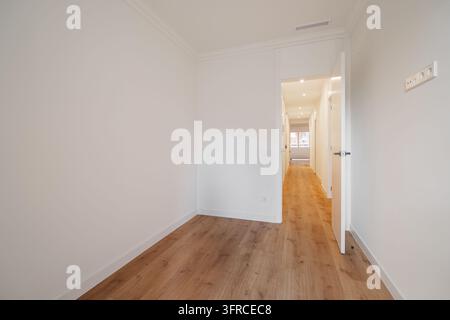 Un couloir lumineux et vide avec des murs blancs et un sol en bois. L'espace est bien éclairé, menant à une zone ouverte en arrière-plan. Banque D'Images