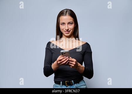Jeune femme souriante tenant un smartphone et regardant la caméra en studio Banque D'Images