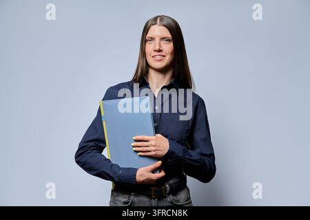 Femme d'affaires souriante tenant un dossier bleu et regardant la caméra en studio Banque D'Images