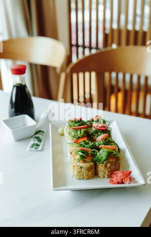 Des rouleaux de sushi frits croustillants garnis de saumon, de salade d'algues et de tomates cerises sont servis avec du gingembre mariné. Représente la cuisine fusion japonaise, res Banque D'Images