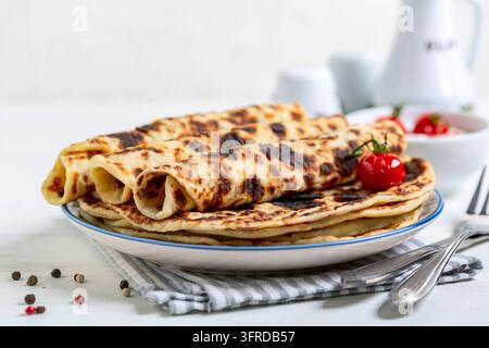 Lefse norvégien traditionnel fait maison – crêpes minces aux pommes de terre avec sauce à la crème fraîche et tomates cerises caramélisées en gros plan, mise au point sélective Banque D'Images
