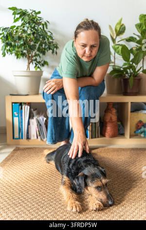 Femme caressant doucement un chien détendu allongé sur un tapis à la maison, entouré de plantes d'intérieur sur une étagère. Mettant l'accent sur la possession et les soins des animaux de compagnie. Une femme adulte Banque D'Images