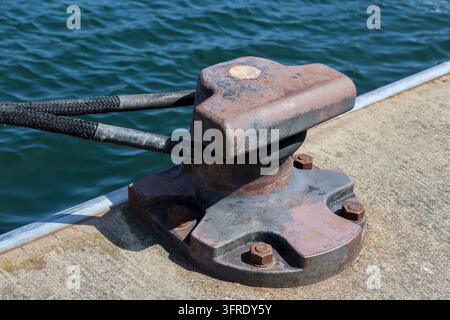 Gros plan d'une borne d'amarrage rouillée tenant une corde épaisse sur une jetée, avec la mer en arrière-plan Banque D'Images