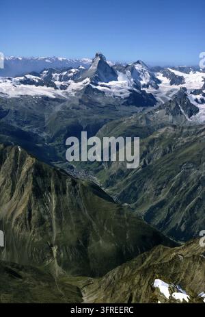Une vue aérienne époustouflante met en valeur l'emblématique sommet du Matterhorn dominant un vaste paysage de montagnes enneigées et de vallées luxuriantes. La scène capture Banque D'Images