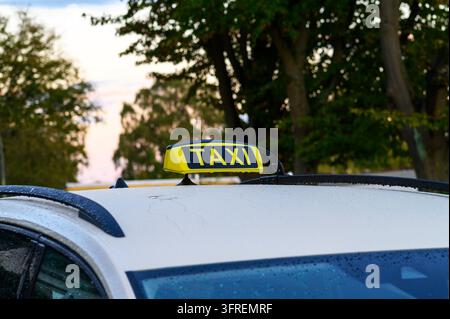 Panneau de taxi jaune monté sur le toit d'une voiture blanche recouverte de gouttes de pluie. Banque D'Images