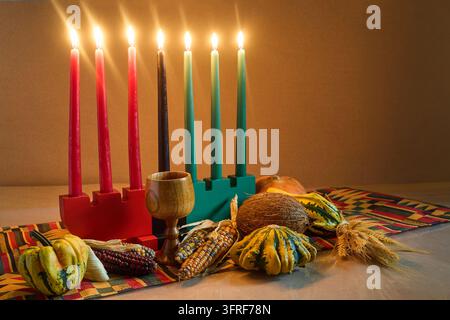 Kinara de Kwanzaa affichant sept bougies allumées et des éléments de récolte sur un tissu africain Banque D'Images
