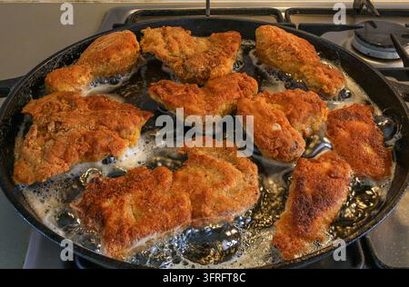 Morceaux de poulet panés dorés grésillant dans une poêle en fonte chaude, produisant une croûte croustillante et friable dans l'huile bouillonnante. Idée de scène de nourriture réconfortante faite maison Banque D'Images