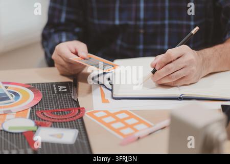 Concepteur travaillant avec des palettes de couleurs, des modèles de mise en page et des outils de conception créatifs sur un bureau tout en planifiant des projets de branding et de conception graphique dans un m Banque D'Images