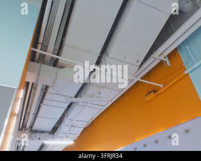 Conduites et tuyaux de ventilation blancs exposés sur un plafond au-dessus d'un mur orange Banque D'Images