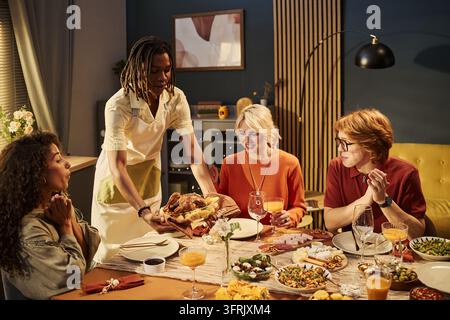 Homme noir servant du poulet rôti à des amis divers autour de la table du dîner Banque D'Images