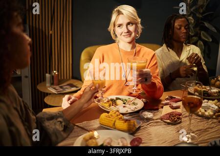 Femme souriante portant un toast avec des boissons auprès d'amis divers lors d'un dîner Banque D'Images