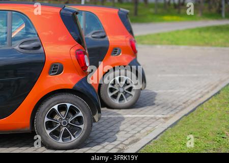 Arrière de deux petites voitures noires et orange dans un parc printanier par une journée ensoleillée - Deux voitures compactes orange et noires garées sur une surface pavée. Les voitures ont un design élégant et moderne Banque D'Images