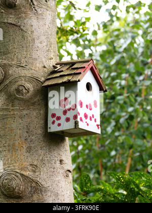 Un nichoir peint en forme de coquelicot sur un tronc d'arbre Banque D'Images